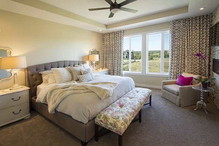 A large bedroom with a recessed ceiling, large window with black out drapes.