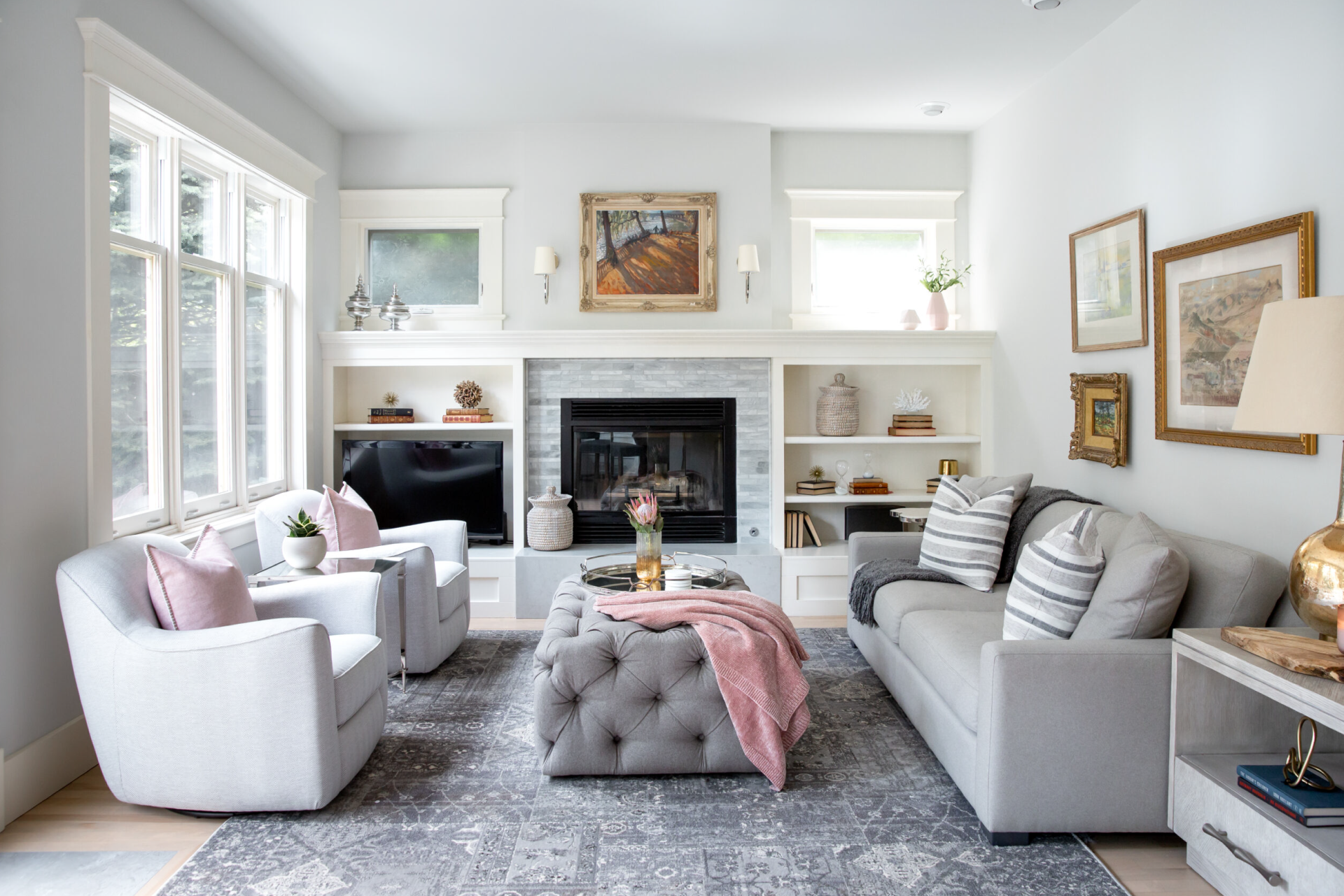 An elegant living room with grey furniture, pink accents, larger windows and an abundance of natural light.