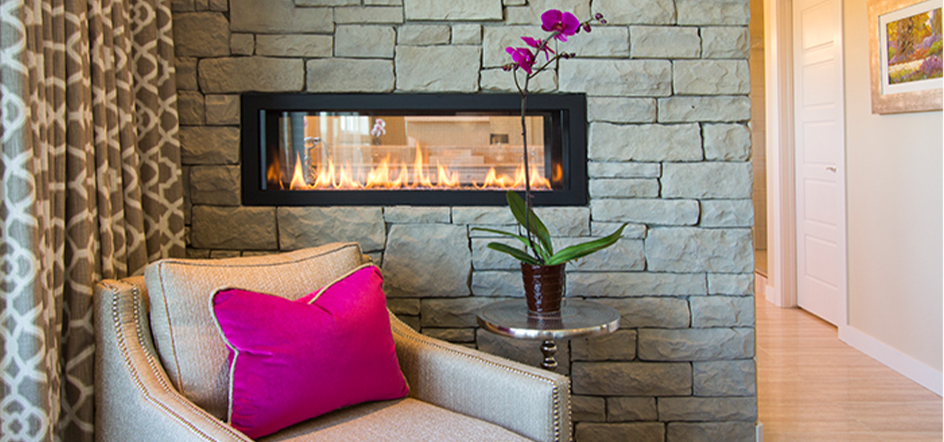 A bedroom nook with a small contemporary gas fireplace in a stone wall.