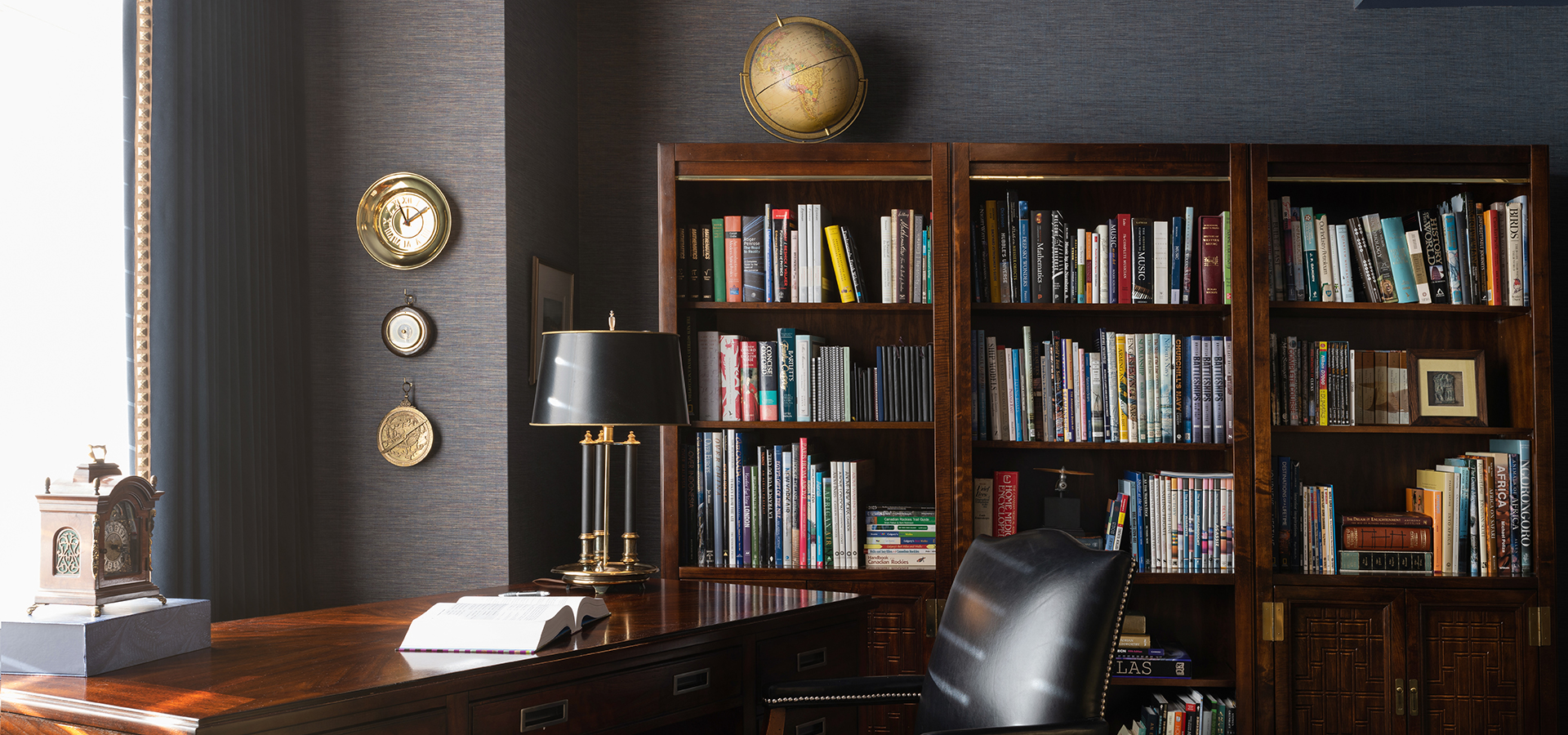 A traditional office with large wood book shelves and black wall paper.