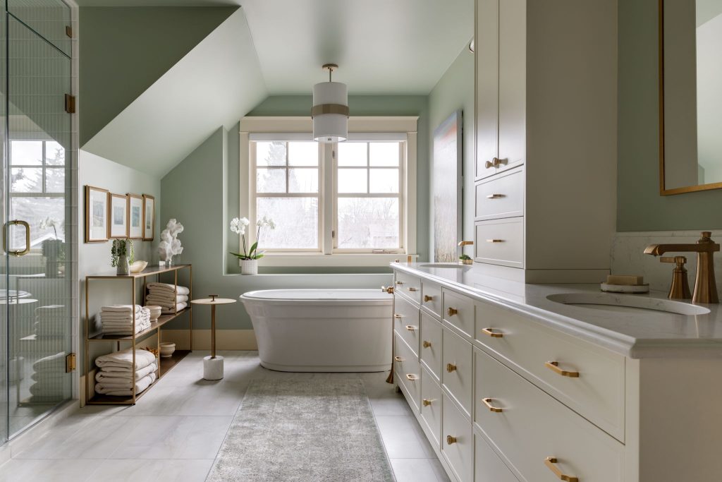 A newly renovated bathroom with a freestanding tub, cream cabinets, a center vanity between two sinks and bronze fixtures.