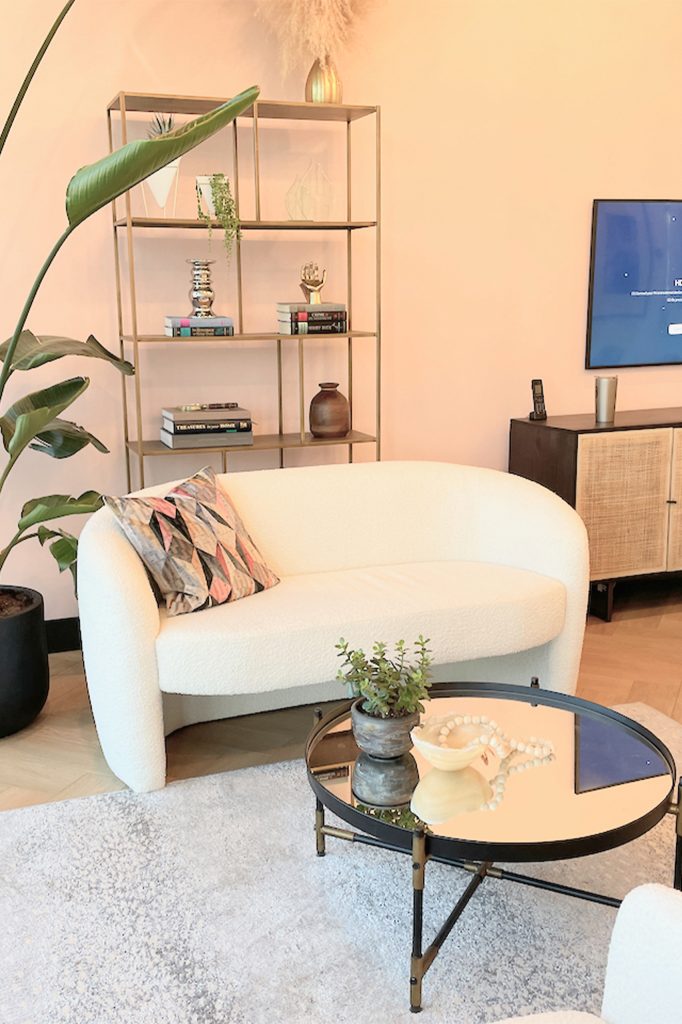 The showroom of a Calgary interior design studio with a modern white sofa, round mirror table, and copper shelving unit.